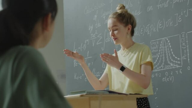 Young girl standing at lectern and talking to group mates during math lesson in college