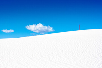 Fototapeta na wymiar Single Red Marker Standing On White Dune With Puffy Cloud In The Sky