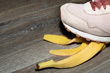 Foot crushing a banana peel on a wooden floor