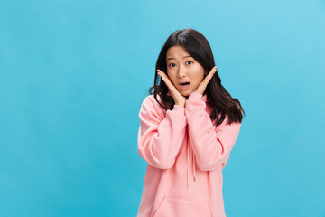 Excited lovely Asian student young lady in pink hoodie sweatshirt recline on hands posing isolated on over blue studio background. The best offer for ad. People Emotions for Everyday concept