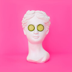 Antique female statue's head with cucumber slices on her eyes isolated on a pink background. 3d contemporary art. Modern design. Beauty concept