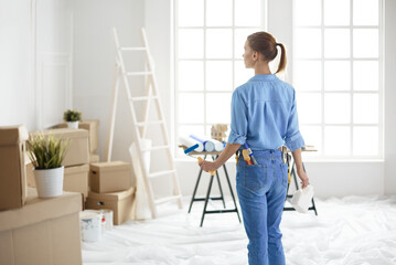 Happy woman paints wall with roller at home