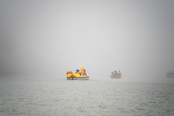 multiple varieties of colorful boats shaped like dragons, sail boats, pedal boats in fog haze...