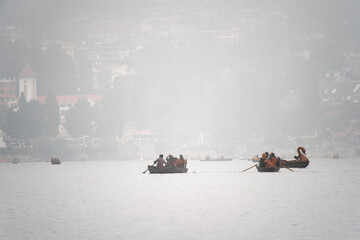 foggy lake at bhimtal filled with row boats piloted by locals carrying tourists come to visit this...
