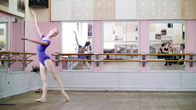 in dancing hall, Young ballerina in purple leotard performs tour chenne on pointe shoes, moves with turns elegantly, at mirror in ballet class. High quality photo