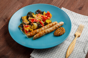 A plate of vegetables with grilled sausages on a table on a linen napkin and a wooden fork.
