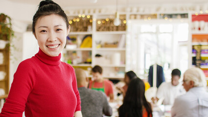 Portrait of attractive Asian teacher smiling to camera in front of her art class, with space for text