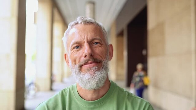 Happy middle aged gray-haired bearded tattooed stylish man standing laughing outdoors. Confident smiling authentic older mature hipster having fun on city street looking at camera, portrait.