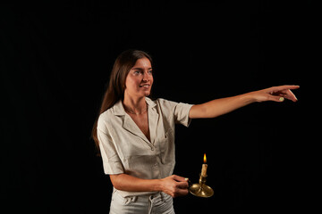 young woman lit by an old brass lamp with a candle on a black background points with her left hand
