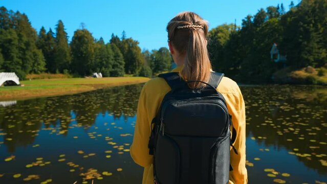 Woman tourist with backpack standing near the lake.
