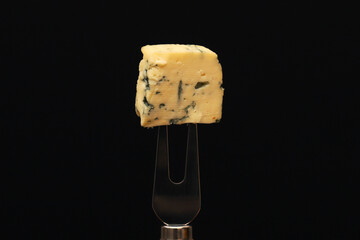 A piece of French blue cheese on a fork on a black background. Close-up