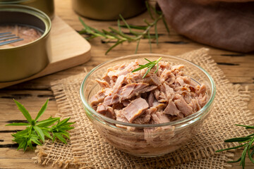 Canned tuna in brine in glass bowl on wooden table