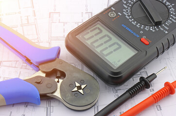 Multimeter and tools for installing an electrical control panel in close-up on an electrical diagram.