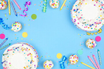 Birthday party frame on a blue background. Overhead view with cakes, party hats and confetti. Copy...