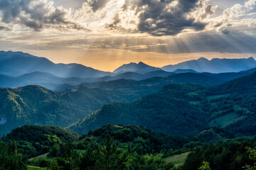 Fototapeta premium Paisaje montañoso rayos de sol durante el atardecer iluminando las montañas y los prados
