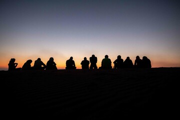 Fototapeta na wymiar A group of people, team work, companions, friends sitting together during sunrise or sunset, silhouette
