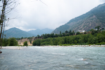 Scenic view of Beas river flowing in background of peaks of Himalayan mountains and dark clouds in...