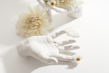 White hands on a white table hold flowers instead of a vase. Original stylish bouquet