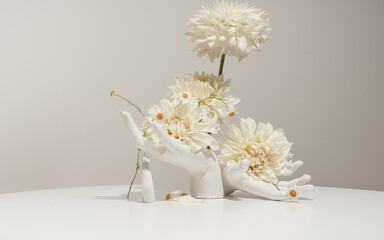 Two white artificial hands on a white table hold a flower arrangement. Modern floristry