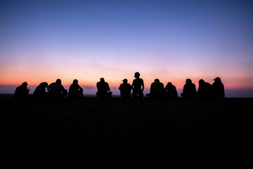 A group of people, team work, companions, friends sitting together during sunrise or sunset, silhouette