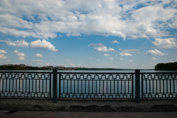 Tranquil lake behind a metal fence, blue sky with white clouds, houses in the distance