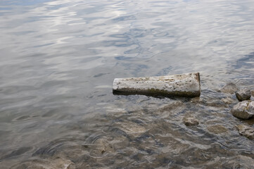 water with small waves, on the shoal lie rocks and an old log