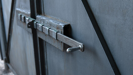 Old gray metal gate with a deadbolt. Shiny polished bolt handle close-up. Traces of corrosion on metal. Aging process. rusty surface. Home security. Outdoors.