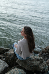 Young woman sitting on the rocks at the wild beach during outcast weather