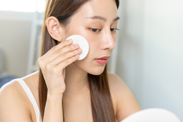 Obraz na płótnie Canvas Happy beauty, beautiful asian young woman, girl smiling, looking in mirror, holding cotton pad, applying lotion by wipe on her face, removing makeup before shower at home. Skin care routine people.