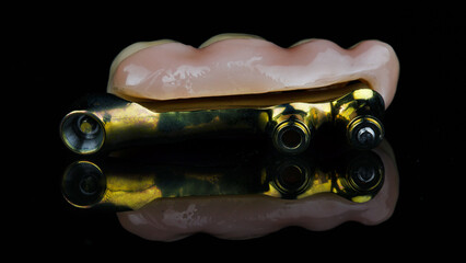 gold-colored bar made of titanium and zircon prosthesis on black glass with reflection