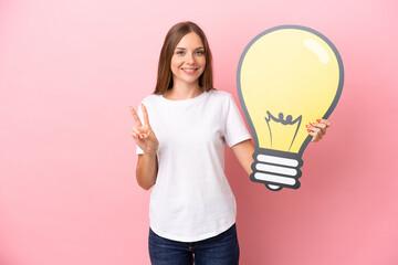 Young Lithuanian woman isolated on pink background holding a bulb icon and celebrating a victory