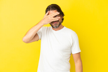 Fototapeta na wymiar Senior dutch man isolated on yellow background covering eyes by hands and smiling