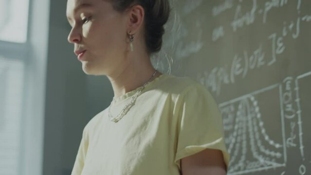 Low angle tilt up shot of young female student giving presentation at lectern during lesson in college