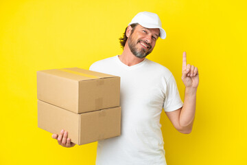 Delivery senior dutch man isolated on yellow background showing and lifting a finger in sign of the best