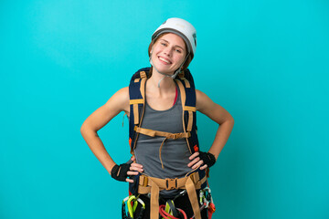 Young English rock climber woman isolated on blue background posing with arms at hip and smiling