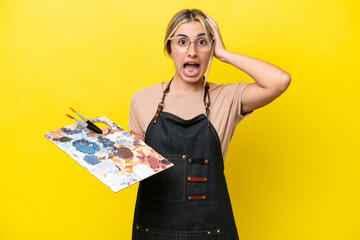 Young artist caucasian woman holding a palette isolated  on yellow background with surprise...