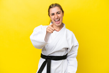 Young caucasian woman doing karate isolated on yellow background surprised and pointing front © luismolinero