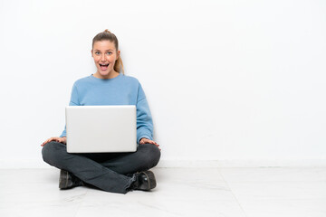 Young woman with a laptop sitting on the floor with surprise facial expression
