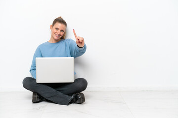 Young woman with a laptop sitting on the floor showing and lifting a finger