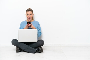 Young woman with a laptop sitting on the floor surprised and sending a message