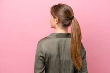 Young caucasian woman isolated on pink background in back position and looking back