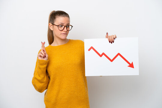Young caucasian woman isolated on white background holding a sign with a decreasing statistics arrow symbol with fingers crossing