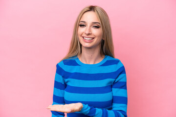 Pretty blonde woman isolated on pink background presenting an idea while looking smiling towards