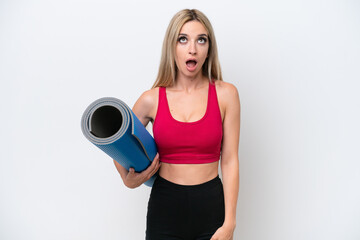 Young sport blonde woman going to yoga classes while holding a mat isolated on white background looking up and with surprised expression