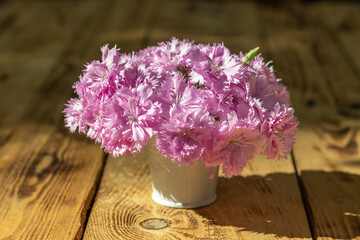 White bucket with pastel pink carnation flowers on a wooden table. Place for an inscription.