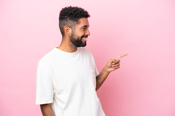 Young Brazilian man isolated on pink background pointing finger to the side and presenting a product