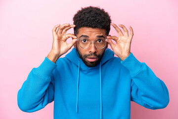 Young Brazilian man isolated on pink background With glasses and frustrated expression