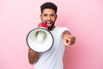 Young Brazilian man isolated on pink background shouting through a megaphone to announce something...
