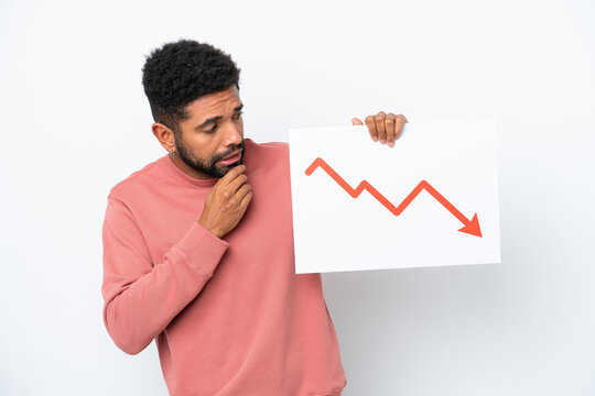 Young Brazilian man isolated on white background holding a sign with a decreasing statistics arrow symbol and thinking