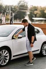 Man is wiping the car with a microfiber cloth. Contactless self-service car wash. Personal car care cleaning outside. Concept disinfection and antiseptic cleaning of vehicle, covid-19 and coronavirus